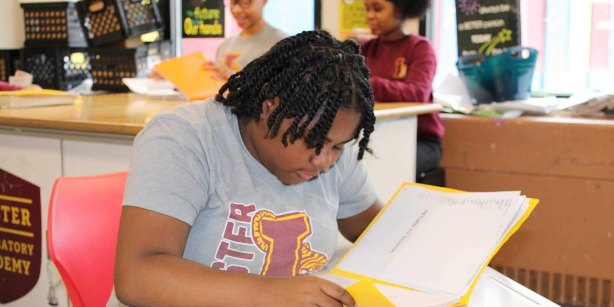 Student reading papers in a yellow folder in a classroom.