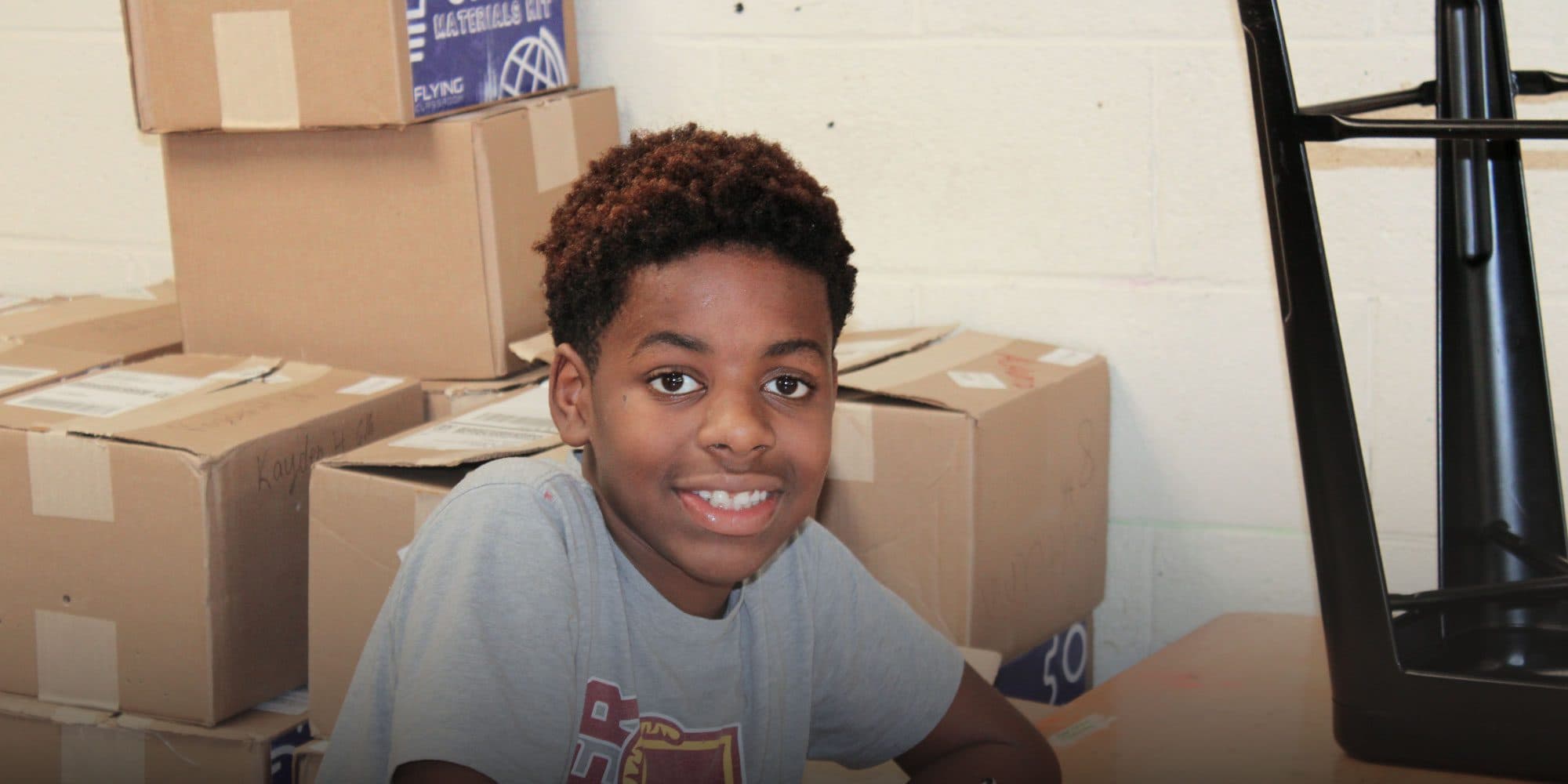 Smiling student sitting in front of stacked supply boxes.