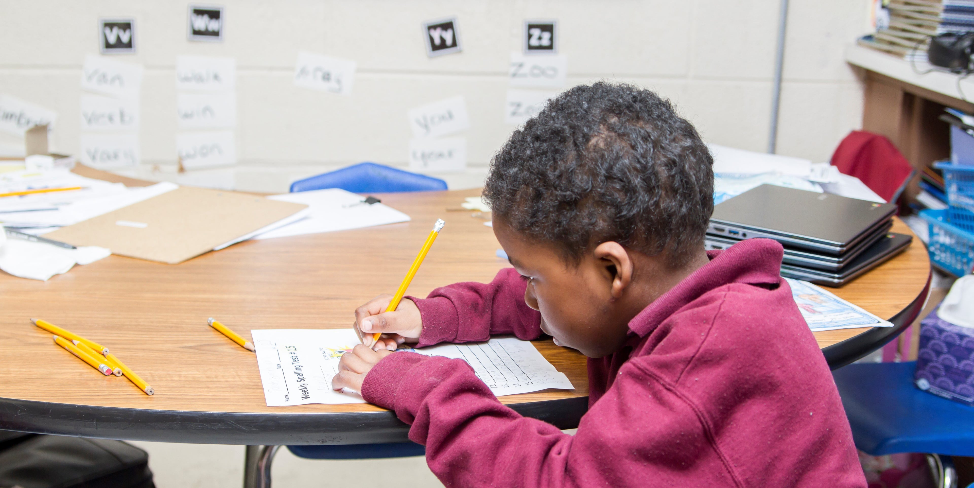 Child writing on a spelling test with a pencil at a table.