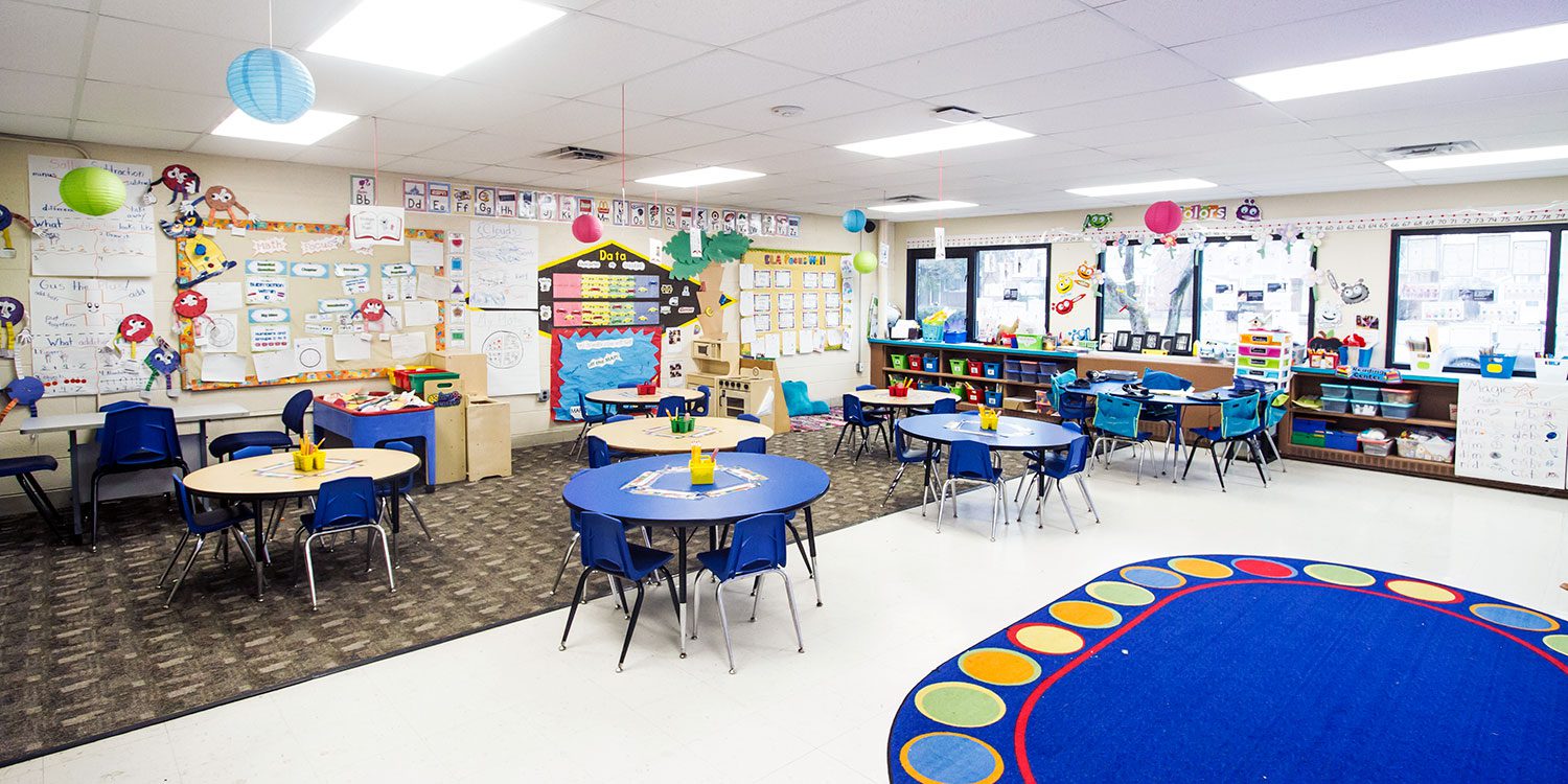 Elementary classroom with bright rug, reading nook and round tables.