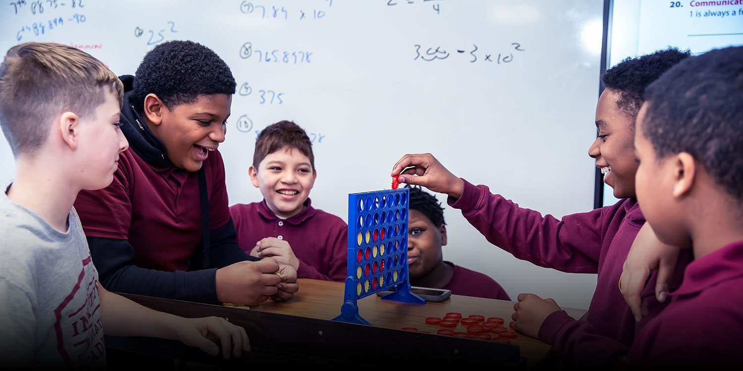 In the classroom, a group of happy students plays connect all four game.